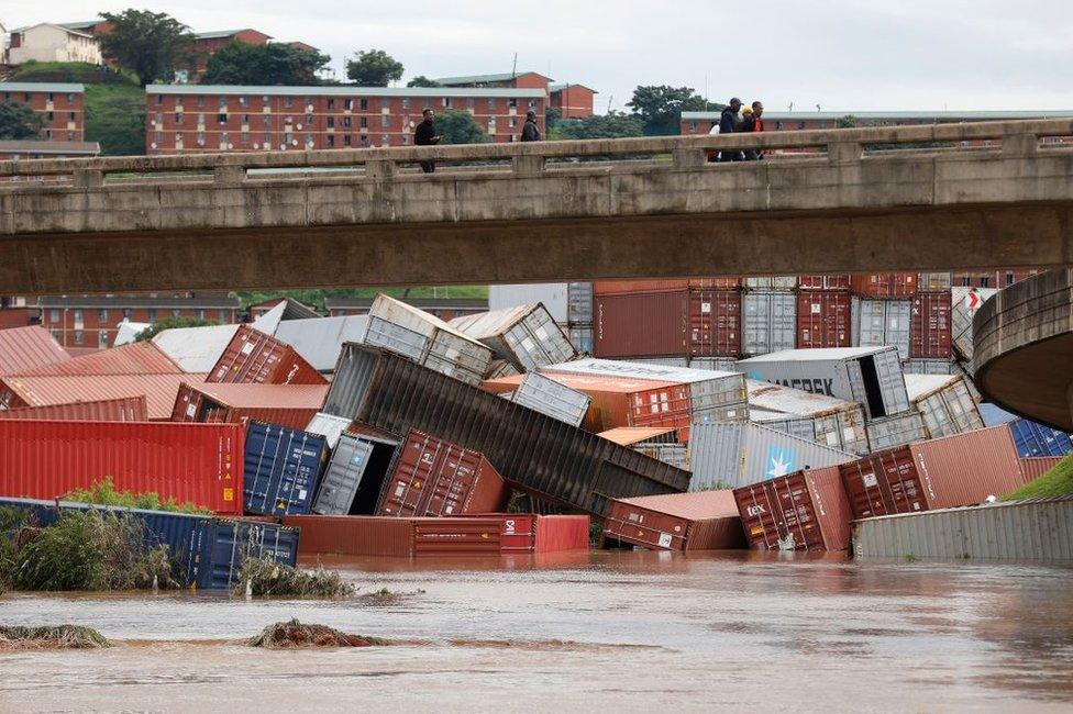 Residents of Umlazi township stand over a bridge and watch containers that fell over at a container storage facility following heavy rains and winds in Durban, on April 12, 2022.