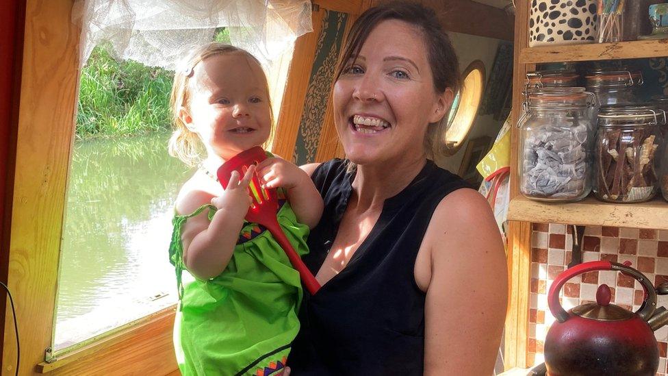 Mary Maw holding daughter Sybil next to their kitchen window on boat "Adrastea"