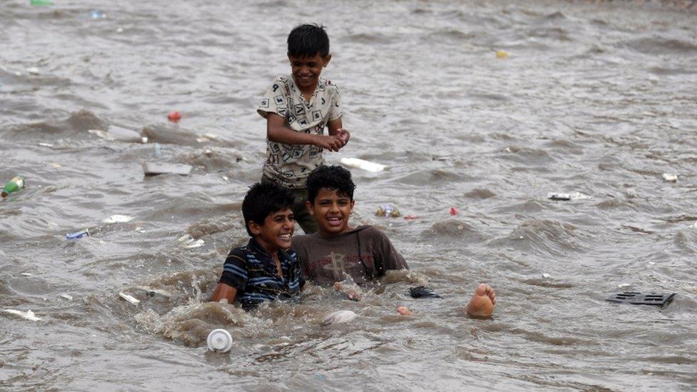 Yemeni boys enjoy rainwater at a flooded street following heavy rainfall in the old quarter of Sanaa