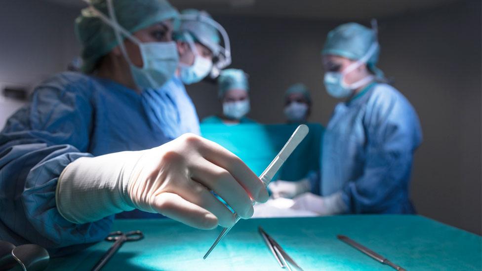 A surgeon lifts a scalpel in a theatre