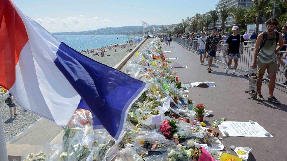 People walk past flowers left in tribute at a makeshift memorial to the victims of the Bastille Day truck attack near the Promenade des Anglais in Nice, France, July 21, 2016.