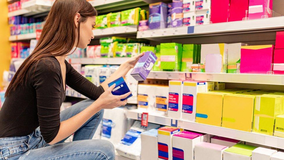 A woman looks at period products in a supermarket