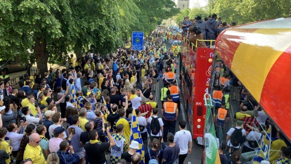 Hundreds of fans line The Plain to cheer for Oxford United as they travel on an open-top bus through the city