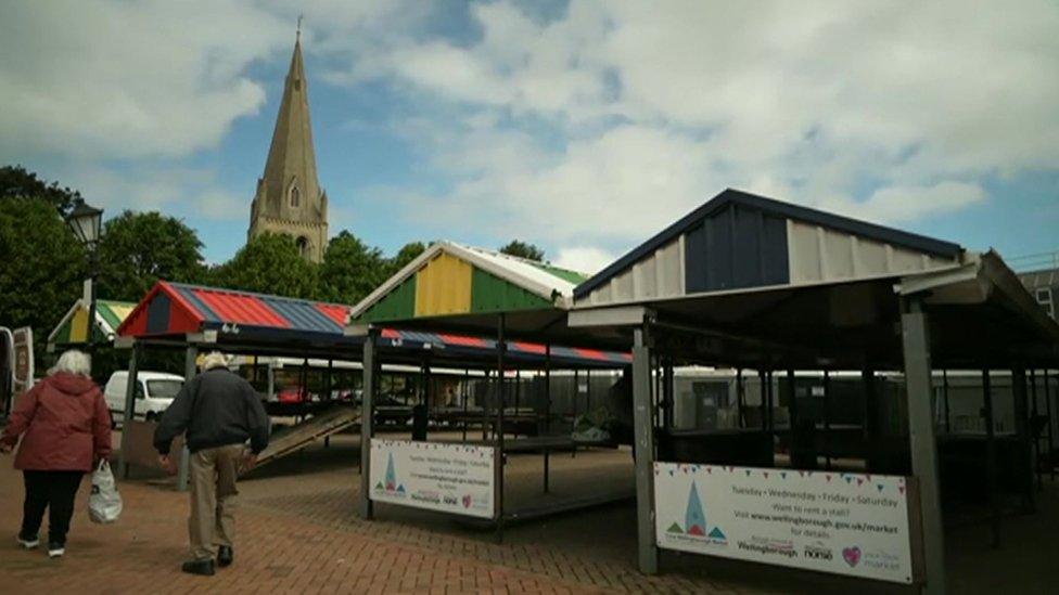 Fixed metal market stalls with shoppers walking past