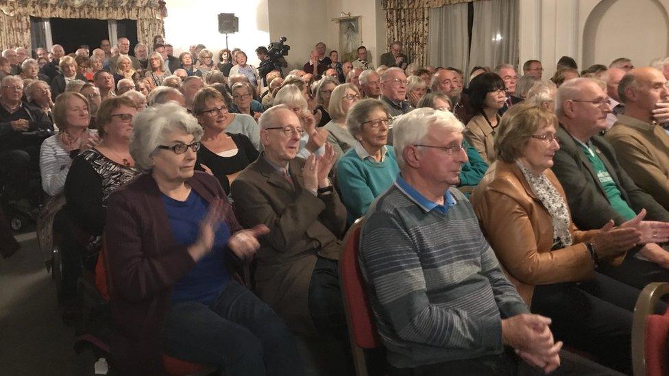 People sitting in a public meeting facing a presentation and clapping