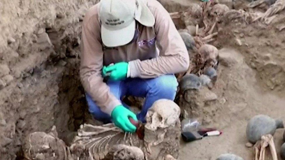 A man dusts off a skull in Chan Chan