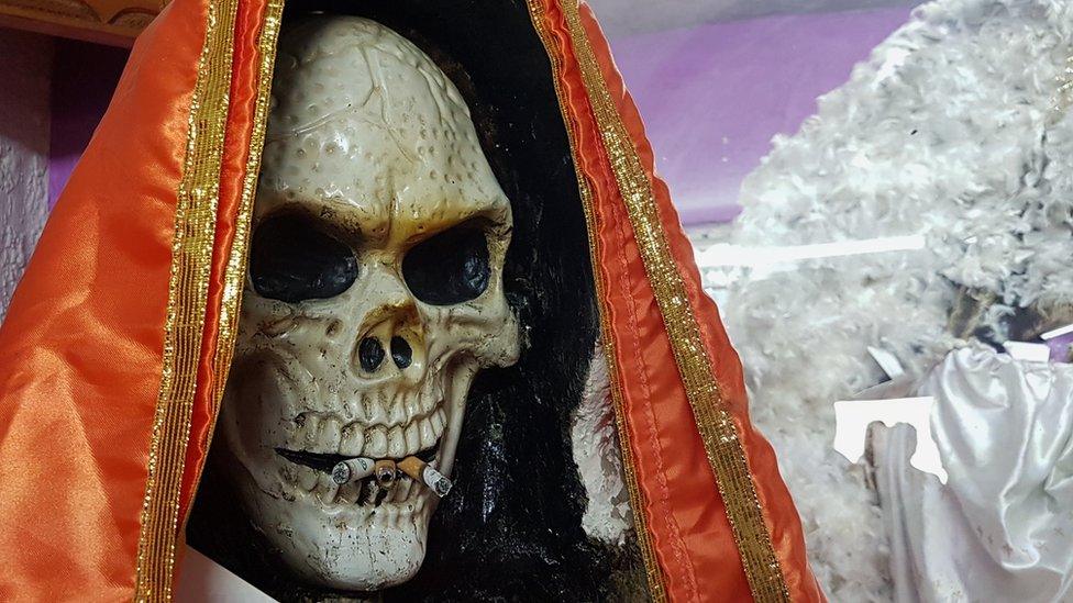 A Santa Muerte statue with cigarettes