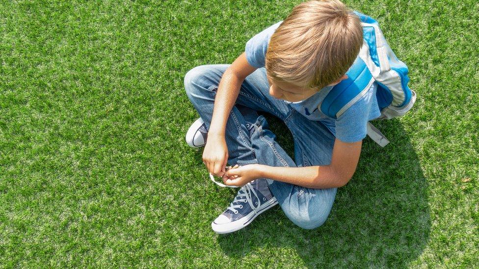 Boy-sitting-on-grasS-with-schoolbag.