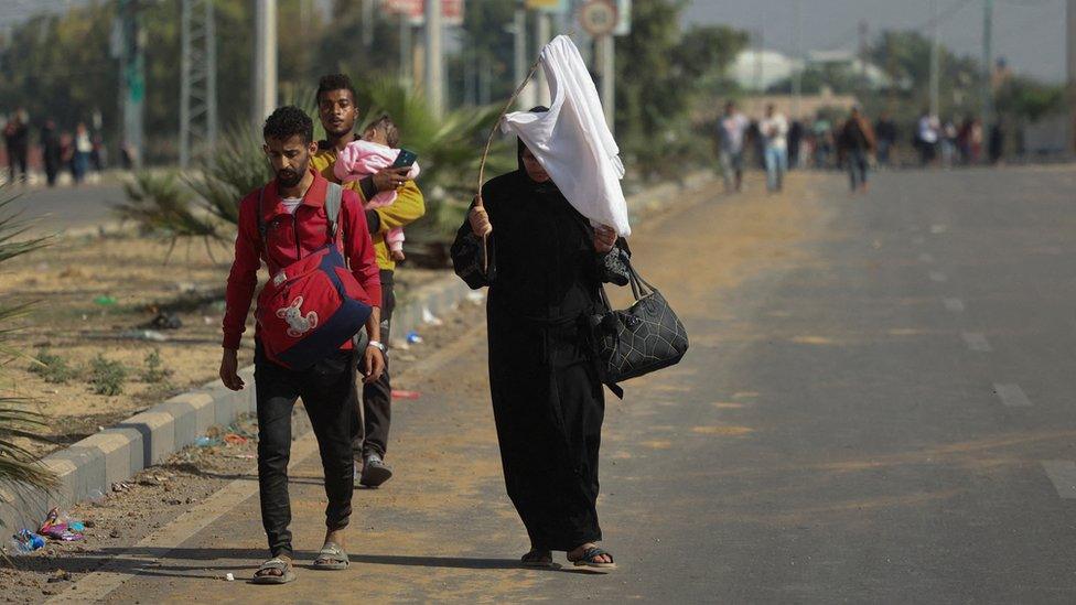 A Palestinian woman holds a white flag while evacuating northern Gaza on foot (7 November 2023)