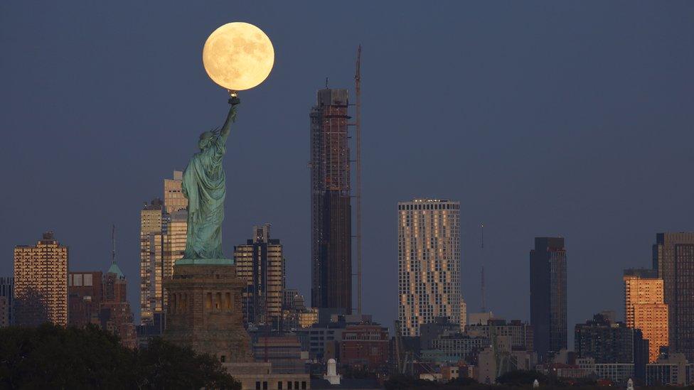 Moon positioned just behind the Statue of Liberty's torch