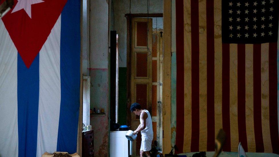 In this Nov. 8, 2016 photo, a U.S. flag and a Cuban flag hang from the wall in the home of actor Armando Ricart while a neighbour cleans a pot in Havana, Cuba