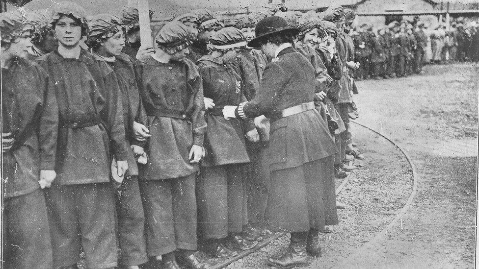 Policewoman assisting munitions workers to look their smartest for a royal visit