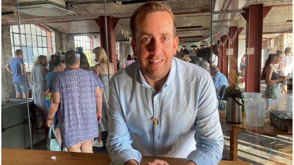 Founder of "The Table", Tom Morgan at The Pattern Church, with people gathering around tables behind him