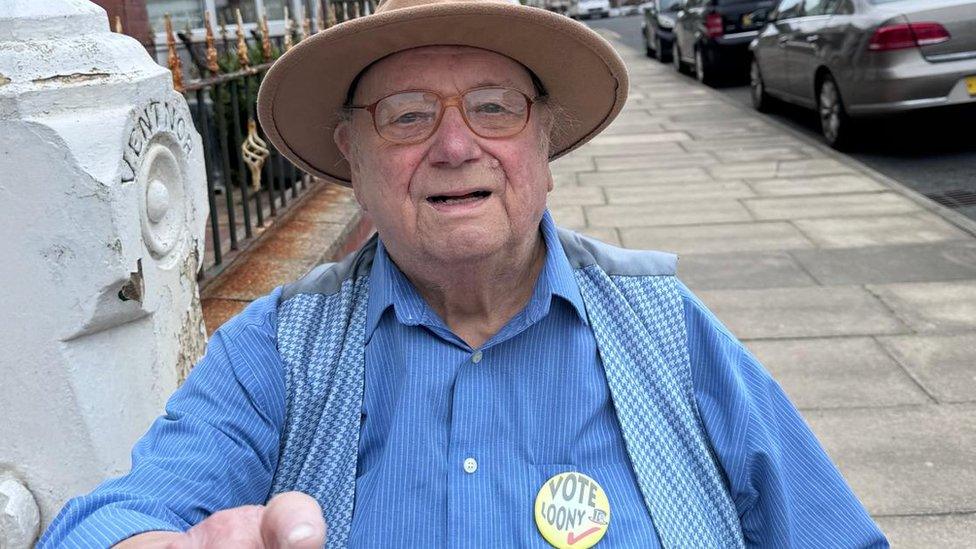 Howling Laud Hope, a white older man in a blue shirt and beige hat smiles into the camera.