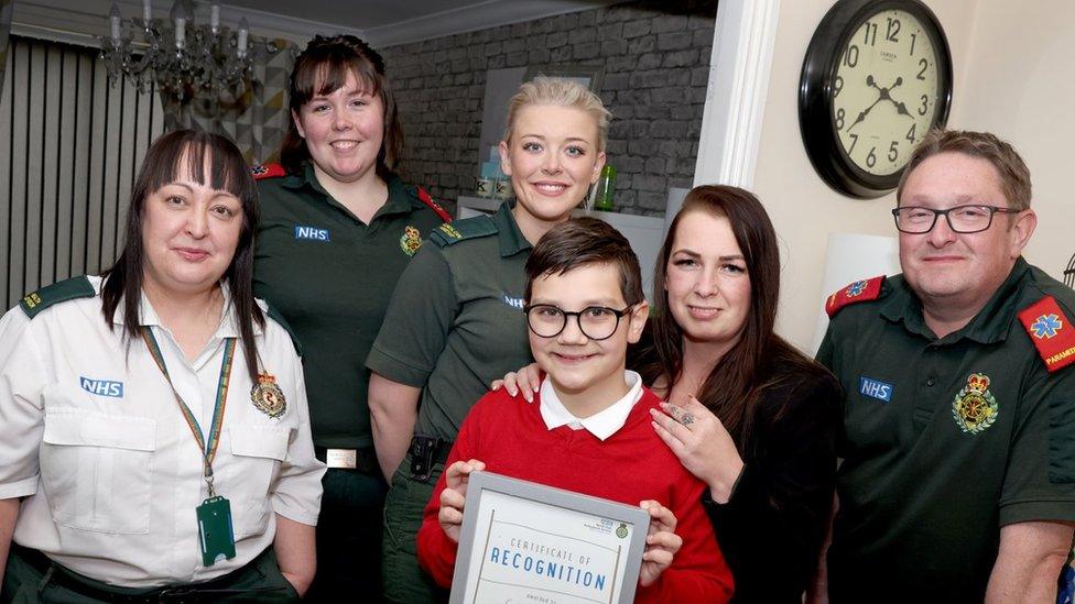 Callum with his mum, certificate and four ambulance staff