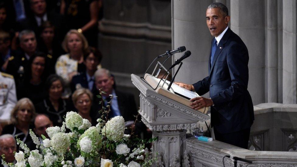 Former US President Barack Obama speaks at the memorial service, from a lectern flanked by white flowers