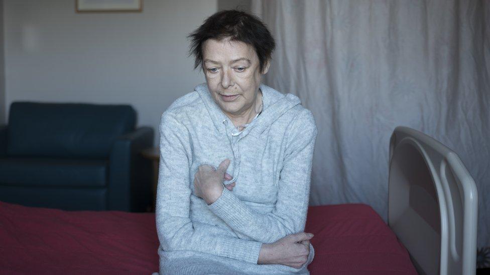 Margaret sitting on her bed with her arms wrapped around herself