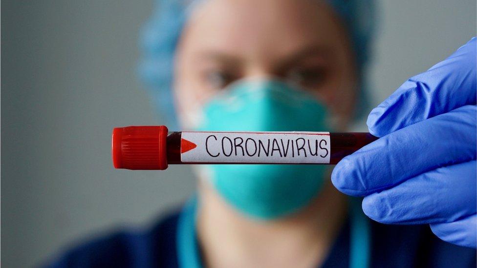 A nurse in protective wear holding a test tube