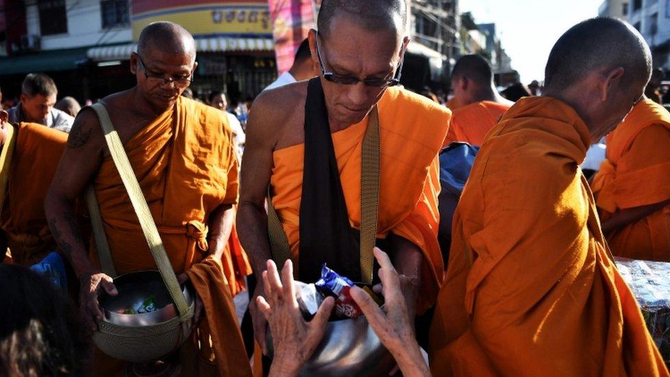 People give alms to Buddhist monks during a mass prayer one week after a lone soldier shot and killed 29 people in Thailand