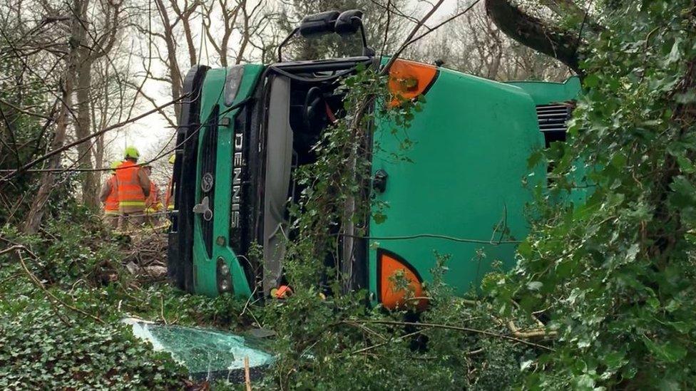 Bin lorry on its side with emergency services personnel on the scene