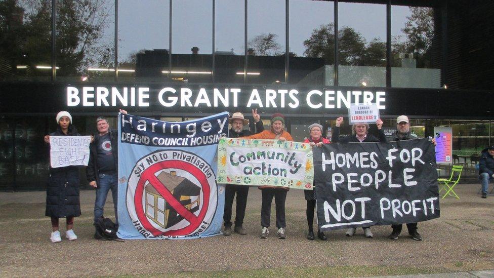 Seven residents holding banners of various colours and sizes, including one saying 'homes for people not profit'