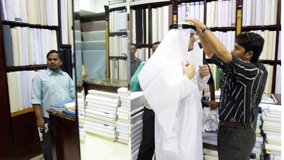 A salesman helps a customer as he tries on a traditional headdress and dishdasha (robe) at a shop in Dubai late September 28, 2008