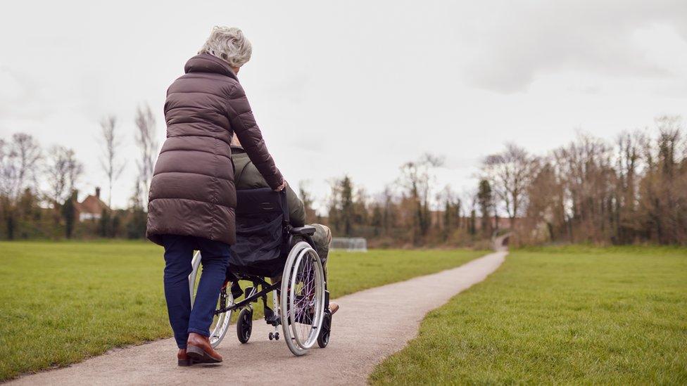 A woman pushing a man who is using a wheelchair