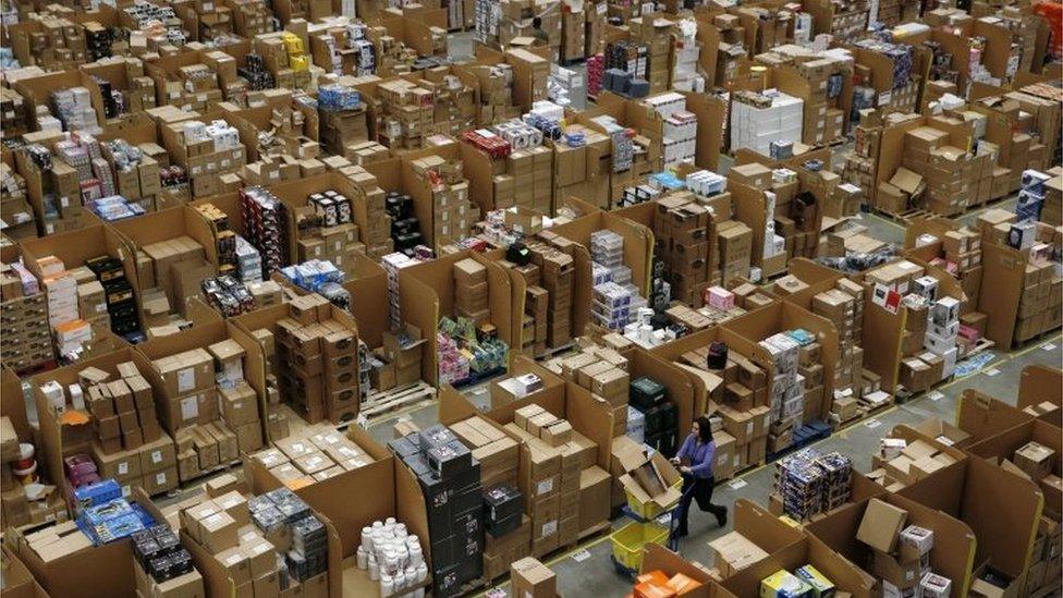 Workers walk along aisles of goods stored inside an Amazon.co.uk fulfillment centre in Hemel Hempstead