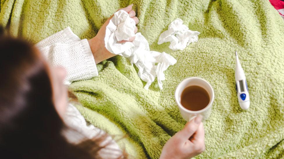 A person at home with tissues and a thermometer