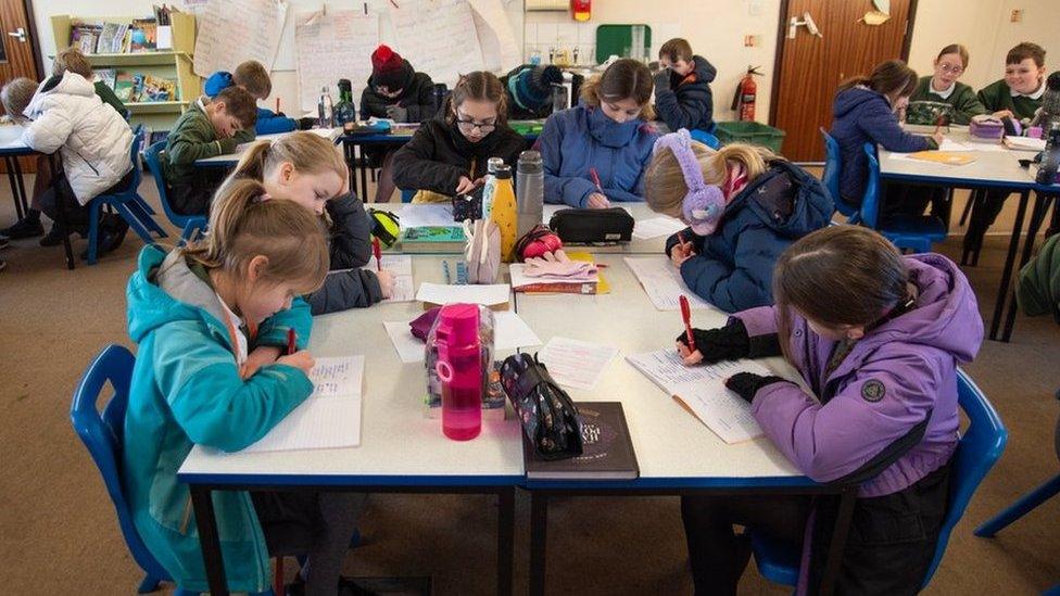 Children wear coats, hats and gloves in their classroom