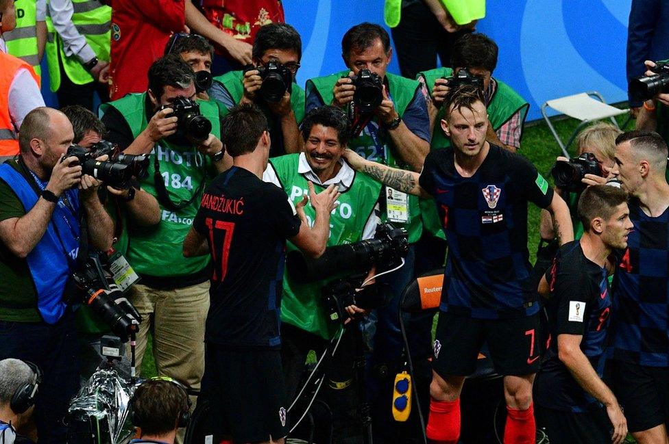 Croatia's forward Mario Mandzukic (L) shakes hands with AFP photographer Yuri Cortez (C) after falling on him with teammates while celebrating their second goal during the Russia 2018 World Cup semi-final football match between Croatia and England at the Luzhniki Stadium in Moscow on 11 July 2018.