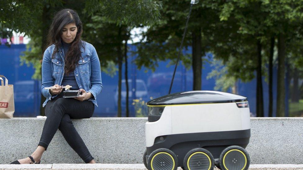 A girl eats takeaway next to a robot