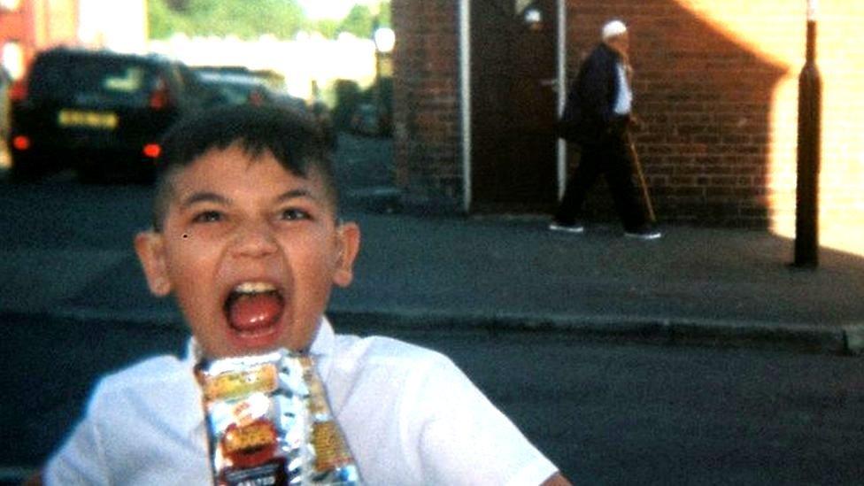 Young boy with bag of crisps (old man in background)