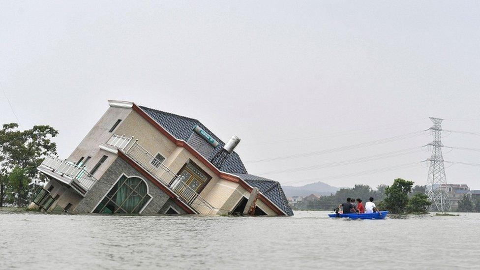 This photo taken on 15 July 2020 shows residents riding a boat past a damaged and flood-affected house near the Poyang Lake due to torrential rains in Poyang county, Shangrao city in China's central Jiangxi province