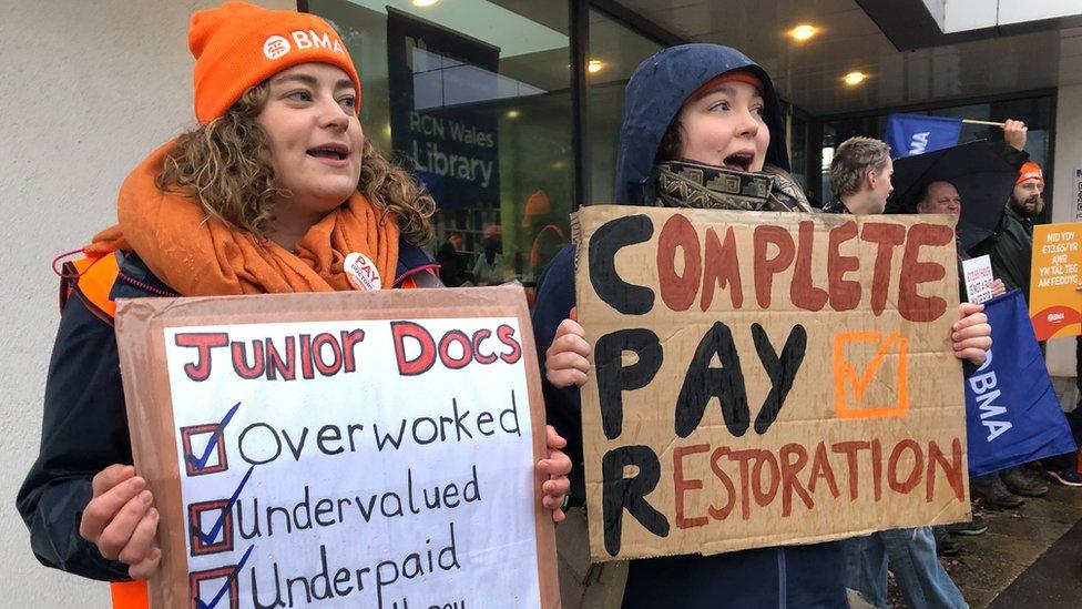 Doctors on strike holding up a placards saying junior doctors are overworked, under valued and under paid