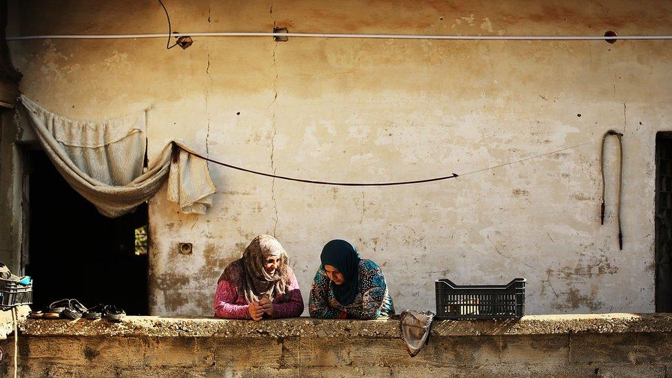 Two women lean on a wall