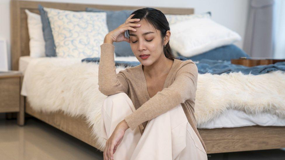 Asian woman sitting on floor next to bed feeling depressed