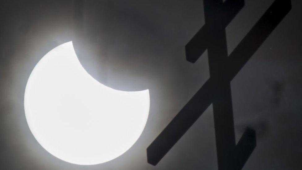 The partial solar eclipse seen behind a cross atop a church in Russia.