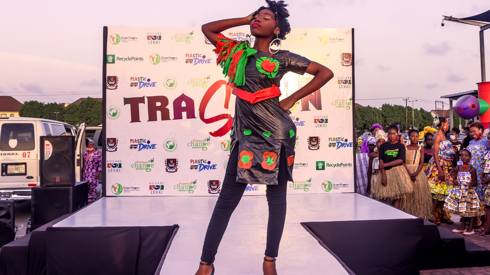 Model posing on runway in black plastic bag dress.