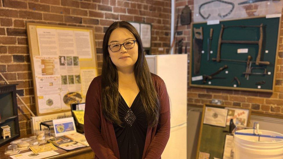 Woman with long dark hair and glasses stands in room full of nature displays