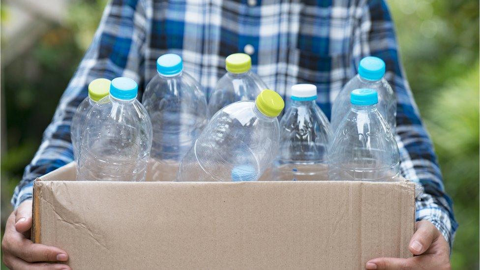 A man carries a box of plastic bottles