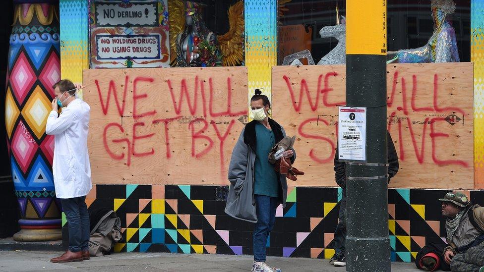 Stuart Malcolm (L), a doctor with the Haight Ashbury Free Clinic, puts on a mask before speaking with homeless people about the coronavirus (COVID-19) in front of a boarded-up shop in the Haight Ashbury area of San Francisco California on March 17, 2020