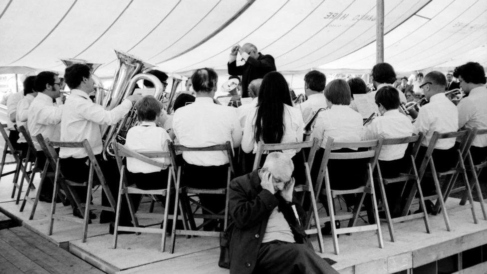 A brass band and a man covering his ears