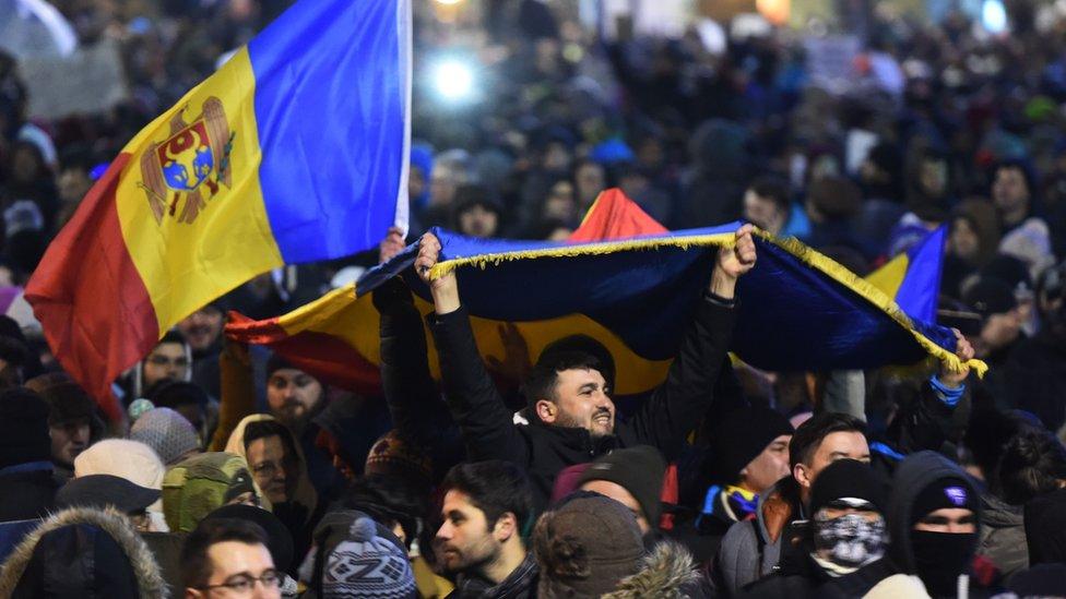 People wave flags during a protest in front of the government headquarters in Bucharest against controversial decrees to pardon corrupt politicians and decriminalize other offenses on February