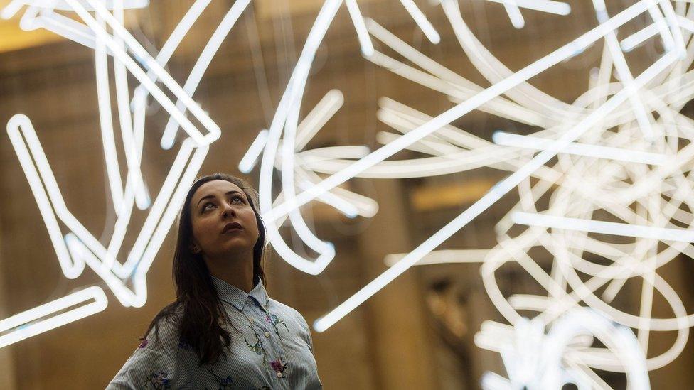 A gallery assistant looks at the neon sculpture