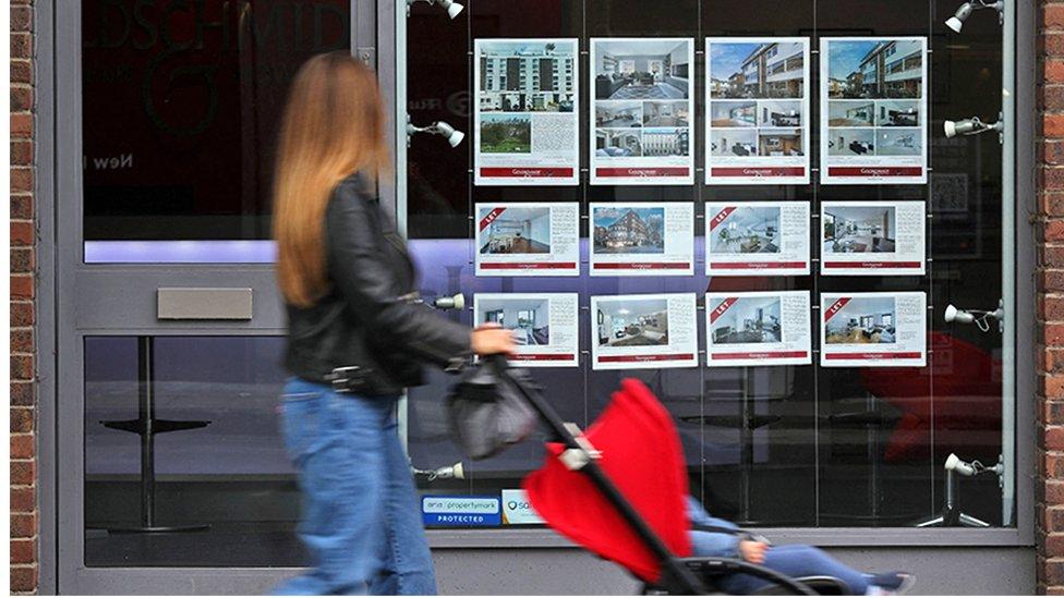 Woman with pram walks past estate agents