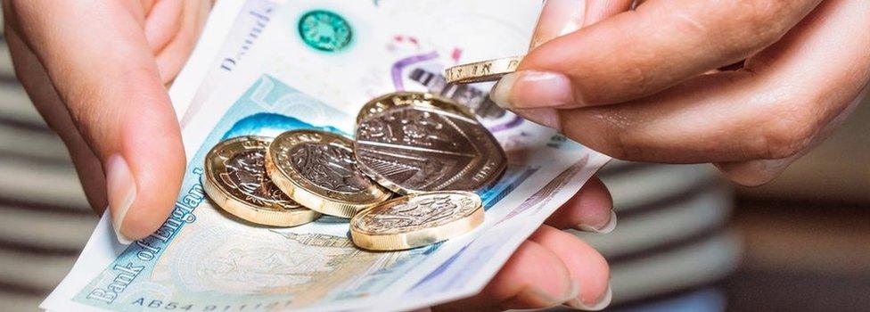 Man holding £5 note and pound coins