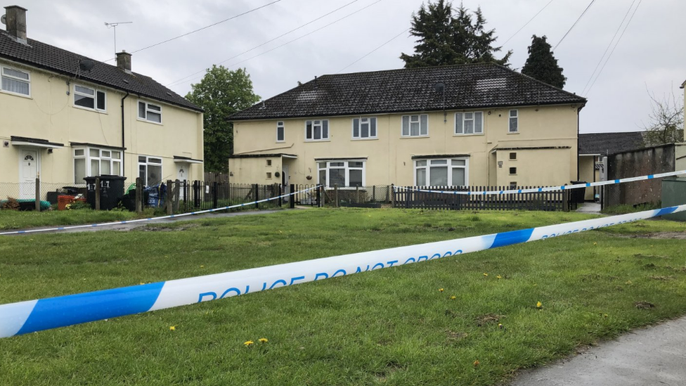 Police tape surrounding an area of grass in front of houses