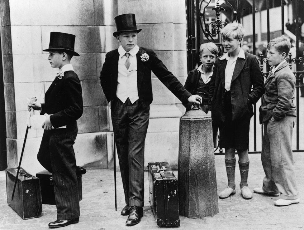 A group of local boys look on with curiosity and amusement at Harrow schoolboys Peter Wagner (left) and Thomas Dyson in their formal uniform at the Eton v Harrow cricket match, held at Lord's cricket ground, London, 1937