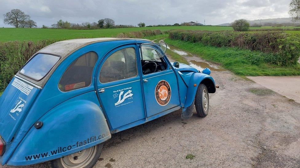 Blue 2CV with b road challenge logo in the entrance to a field